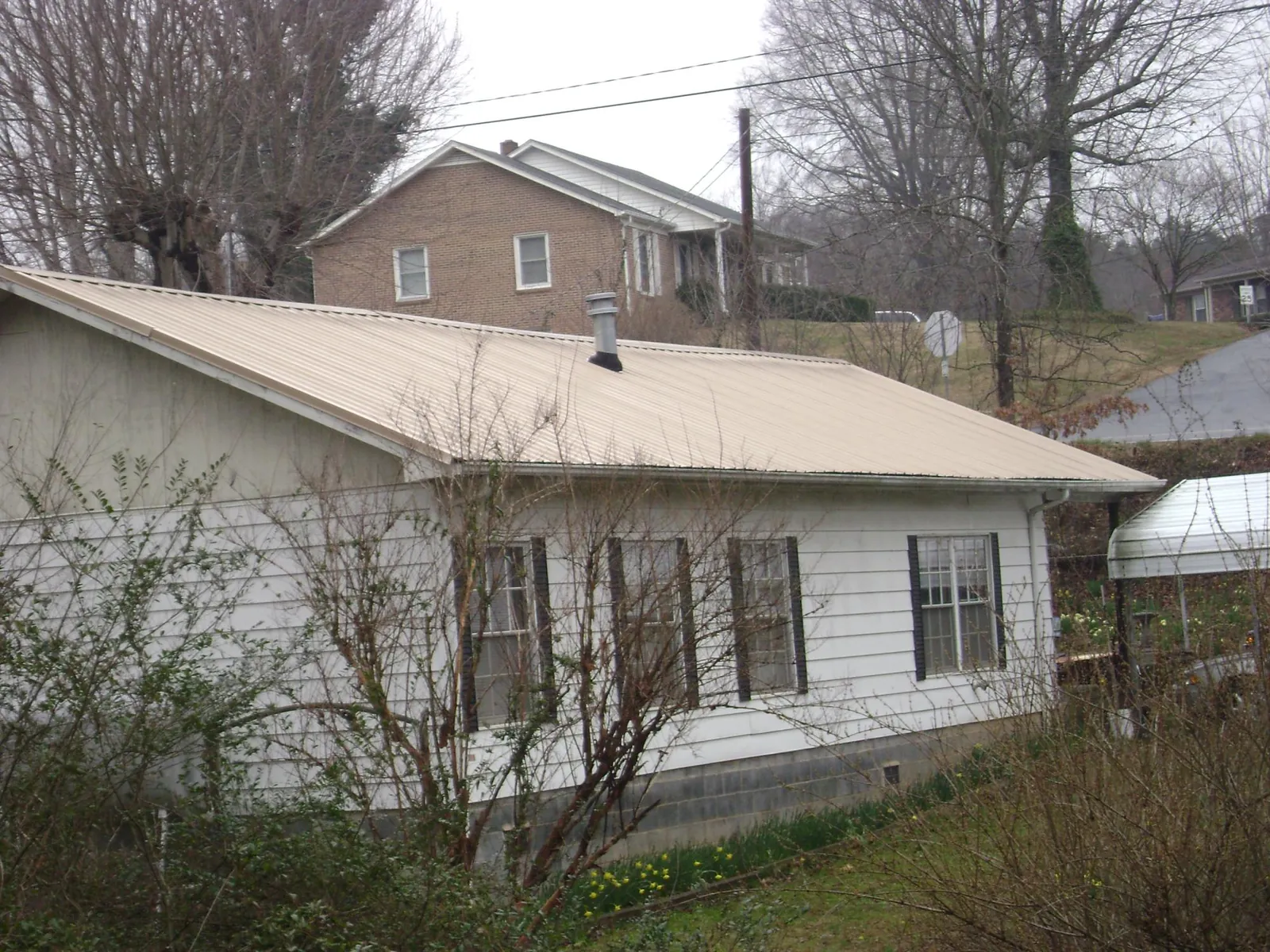 Tan metal roof on a white sided house set into a hillside — Commercial Roofing by Roofing Brothers in Martin